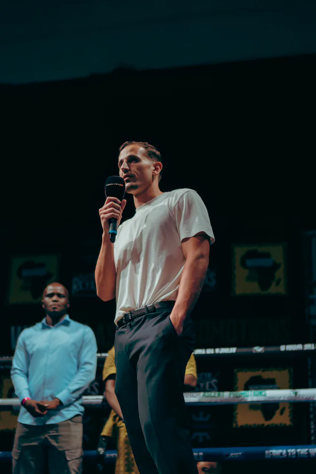 Brad Dayan Norman speaks into a microphone inside a boxing ring.