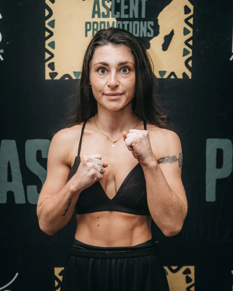 Hanna Von Wirth faces the camera with both fists raised before a Warrior Ascent backdrop