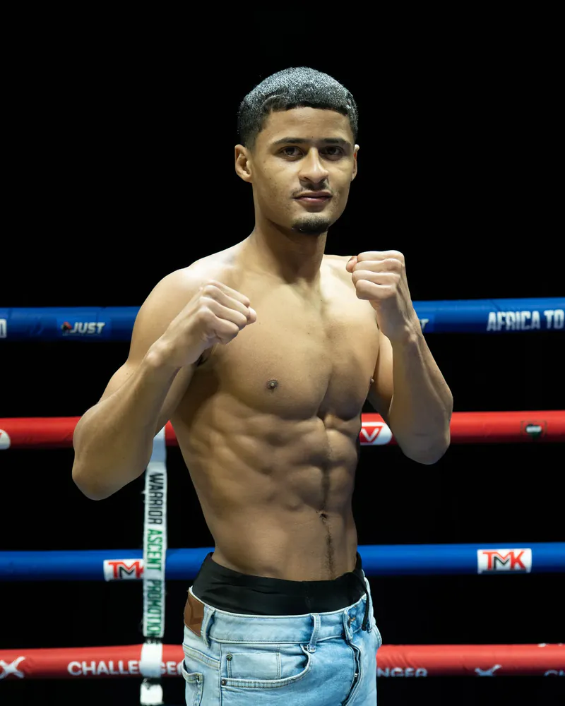 Mika-eel Jacobs poses with both fists raised inside a boxing ring