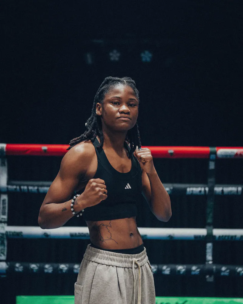 Tarisai Mutsau poses with both fists raised in a boxing ring
